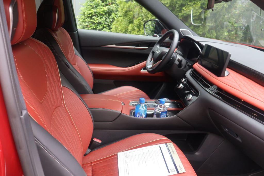 The interior of a red luxury vehicle, with a dashboard, steering wheel, and red leather seats visible. A bottle of water and some papers are on the center console.