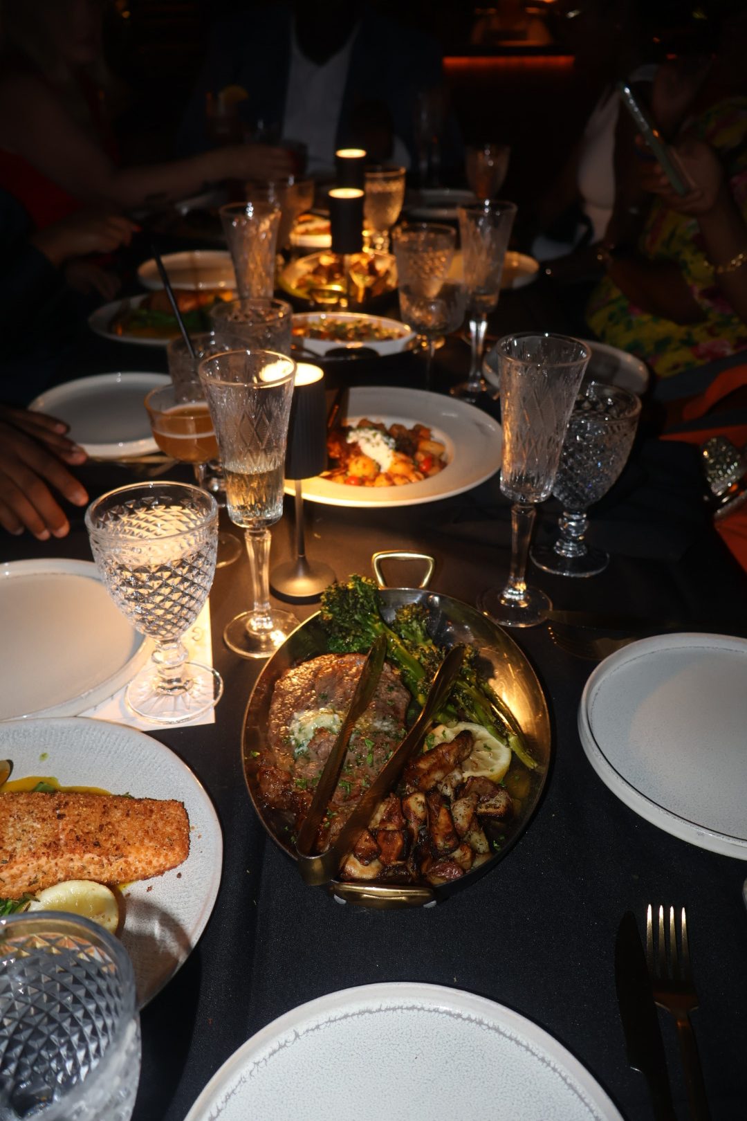 A table set for a formal dinner, with plates, glasses, and a large dish of roasted meat and vegetables in the center.
