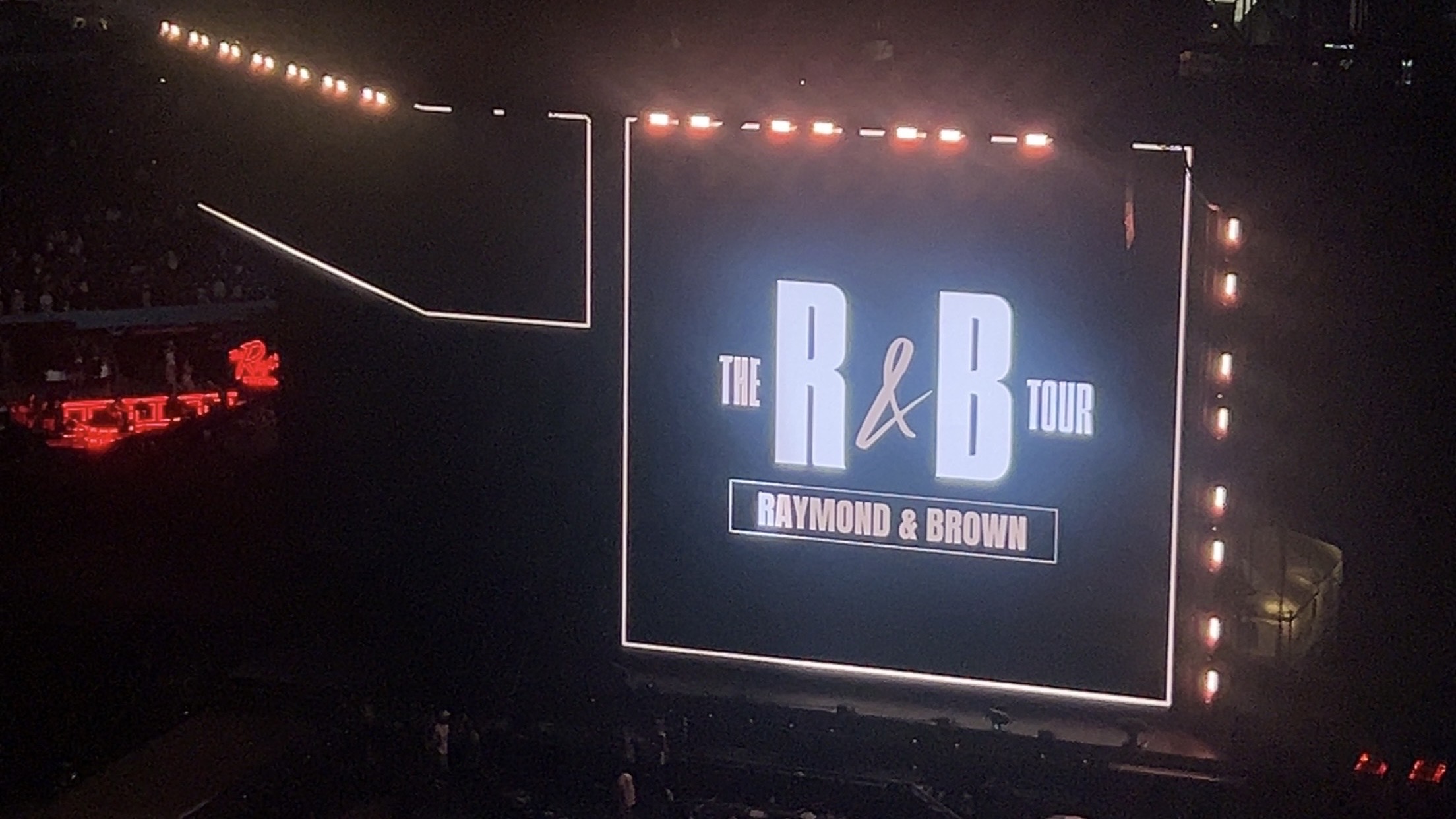 A large stage display showing the text "The R&B Tour" and "Raymond & Brown" in a dark concert venue.