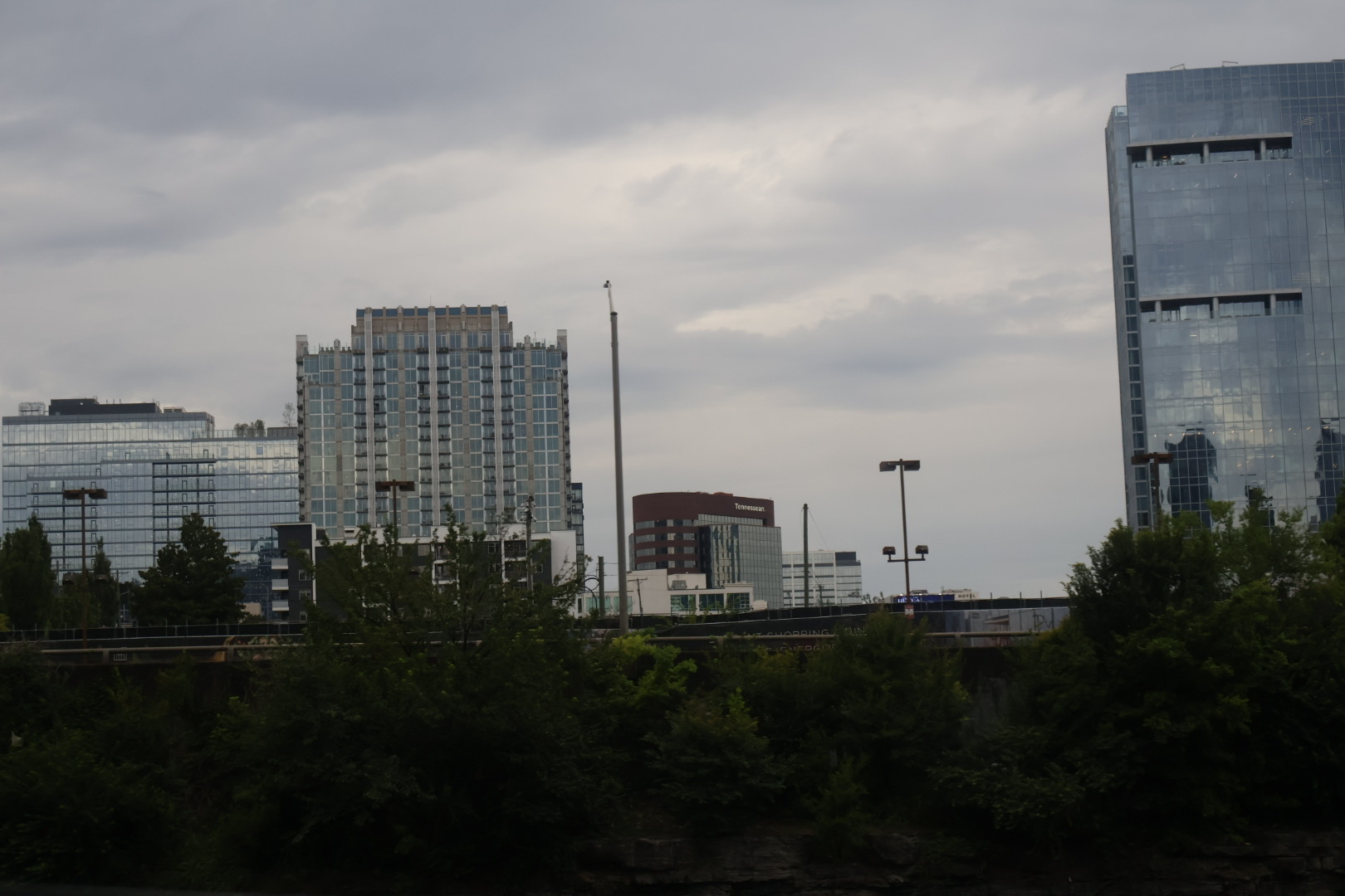 Cityscape with high-rise buildings, trees, and cloudy sky.