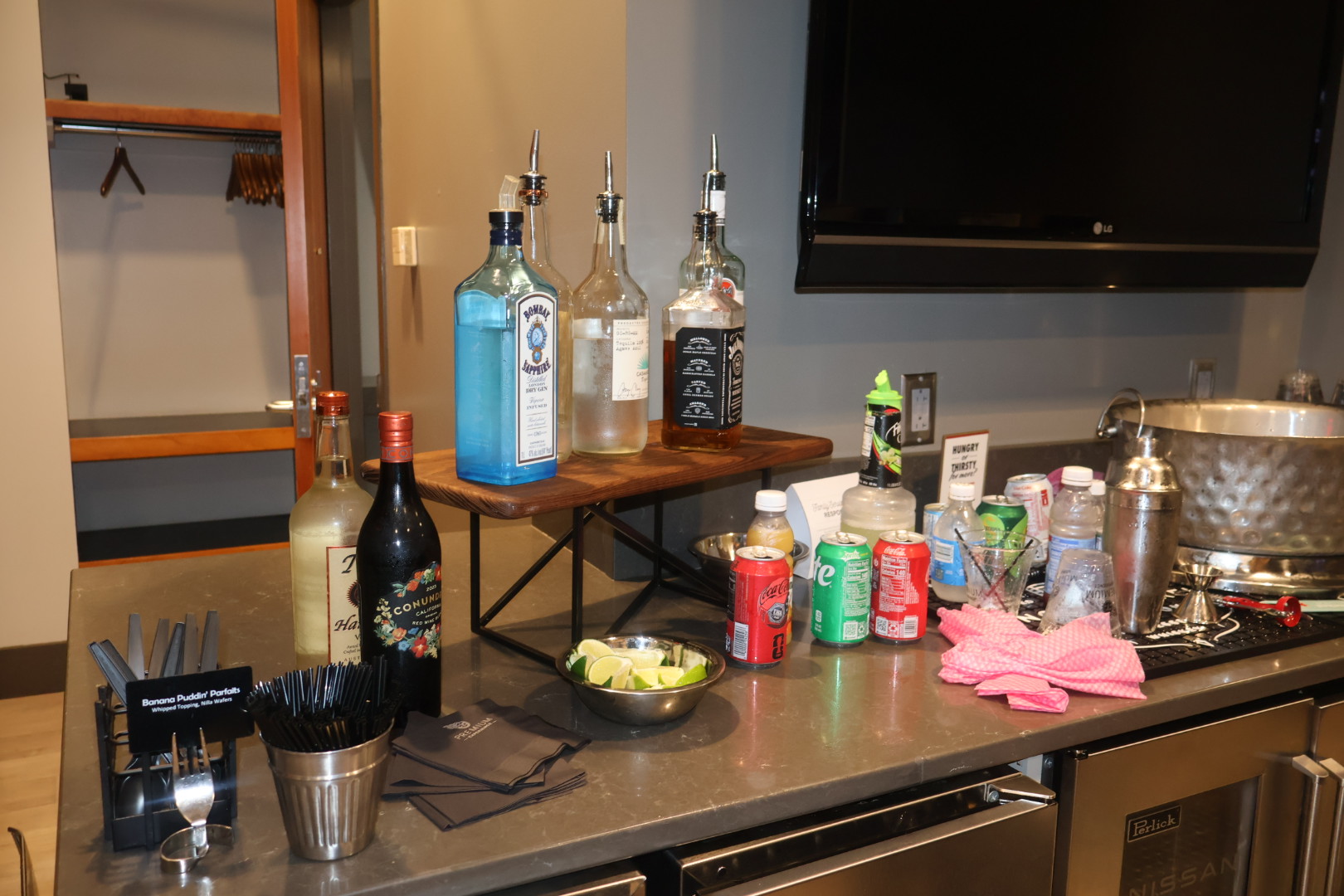 A kitchen counter with various liquor bottles, cans, and other kitchen items. The counter also has a TV visible in the background.