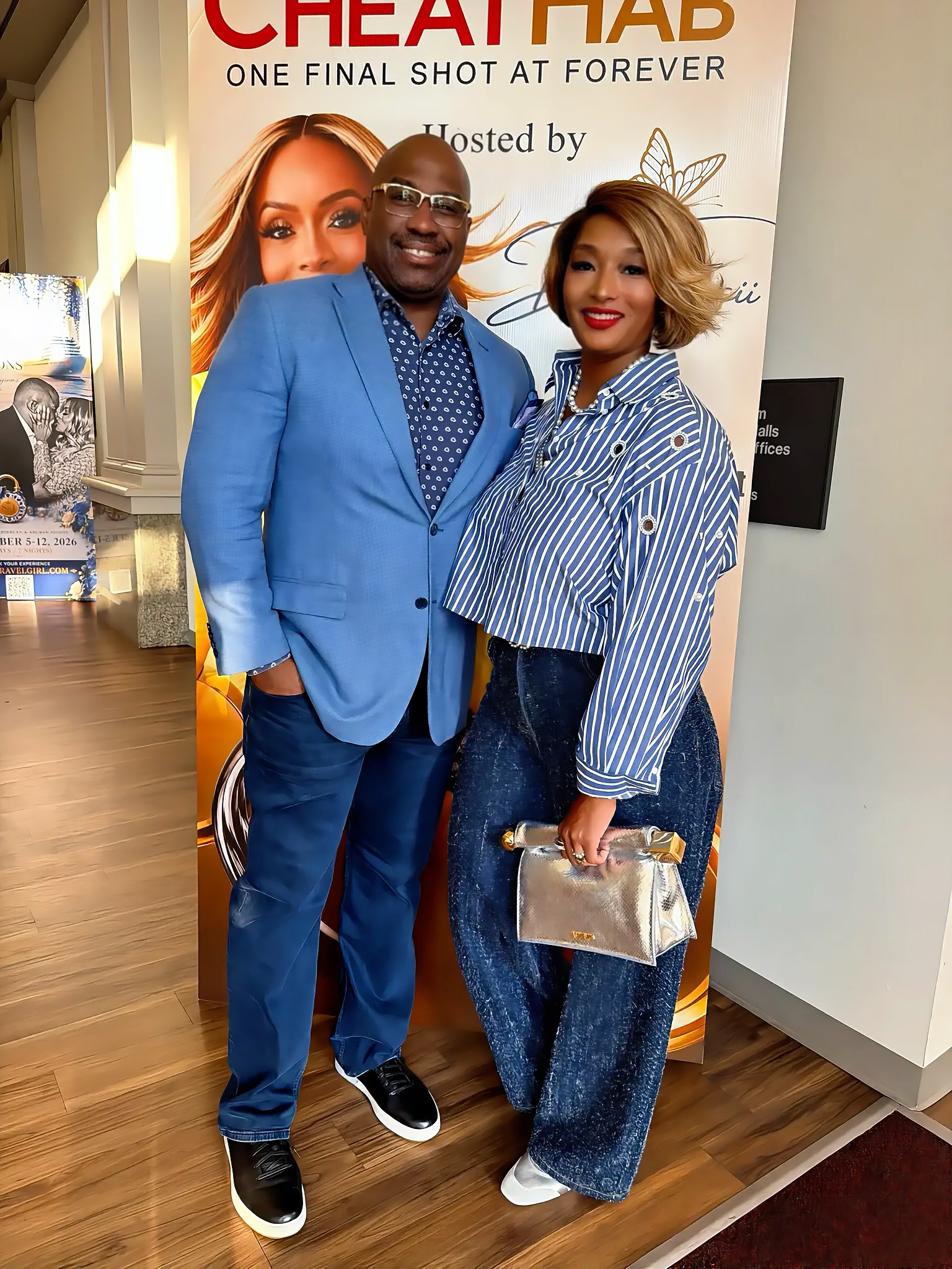Two well-dressed individuals, a man in a blue suit and a woman in a striped blouse, posing in front of a banner for "Cheat Pad: One Final Shot at Forever" event.