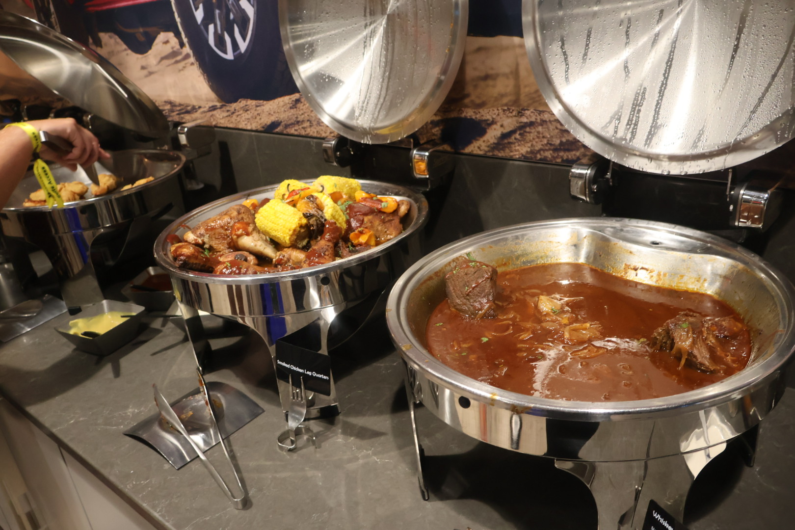 Stainless steel food warmers containing various hot dishes, including a stew or chili with meat and vegetables.