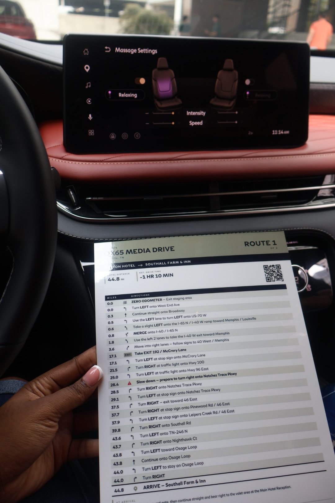 A car dashboard display showing massage settings for the front seats, including intensity and speed controls. Below is a detailed driving route with directions and mileage.