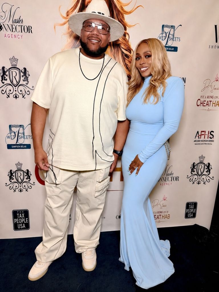 A man and woman posing together at an event, the woman wearing a blue dress and the man wearing a white outfit with a hat.