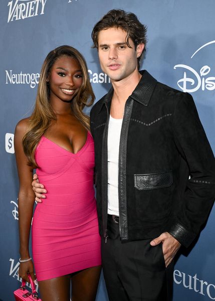 Two people posing on a red carpet at an event, a woman in a pink dress and a man in a black jacket.