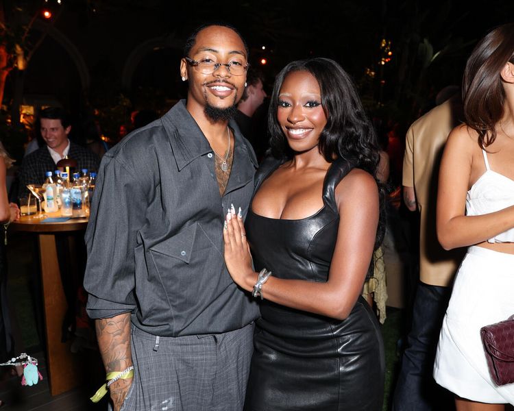 Two people, a man and a woman, posing together at an event. The man is wearing a gray jacket and the woman is wearing a black leather dress.