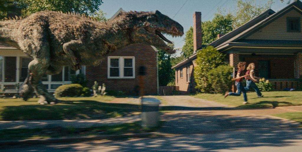 A large dinosaur looming over a residential neighborhood, as two people run away in the foreground.
