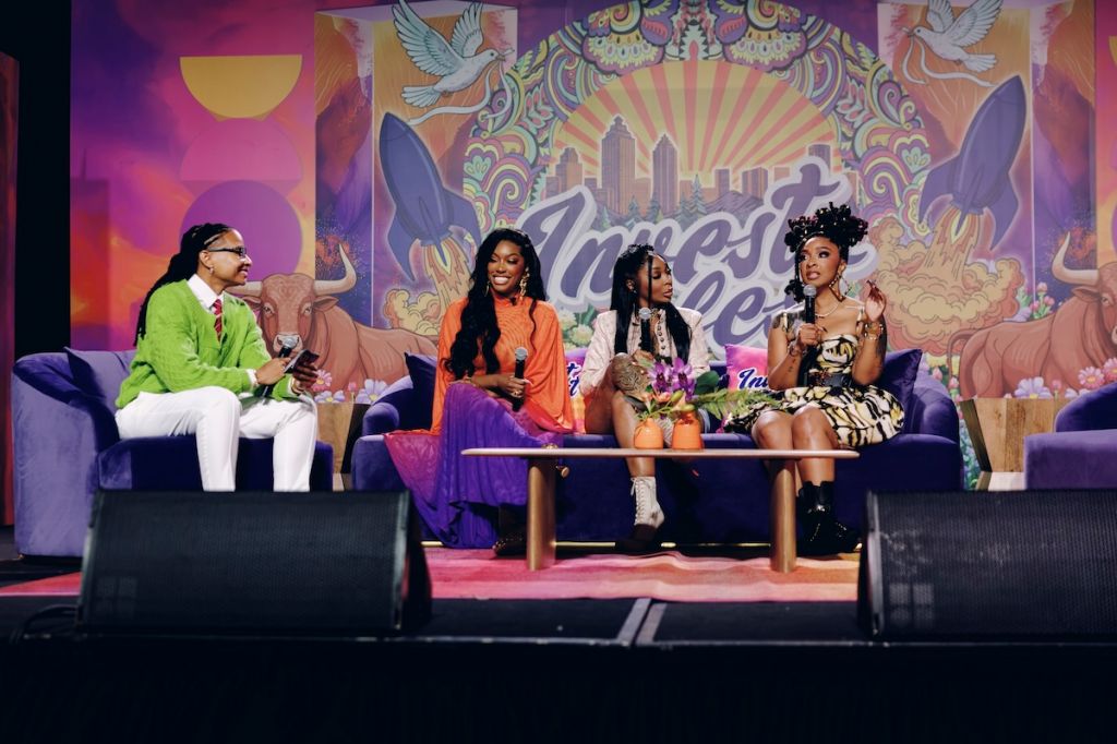 Four people sitting on a colorful, patterned stage set with a cityscape backdrop and winged figures.