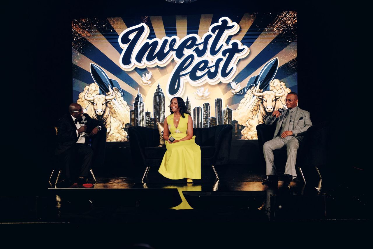 A stage with the text "Invest fest" and a cityscape backdrop. Three people, two men and one woman, are seated on the stage.