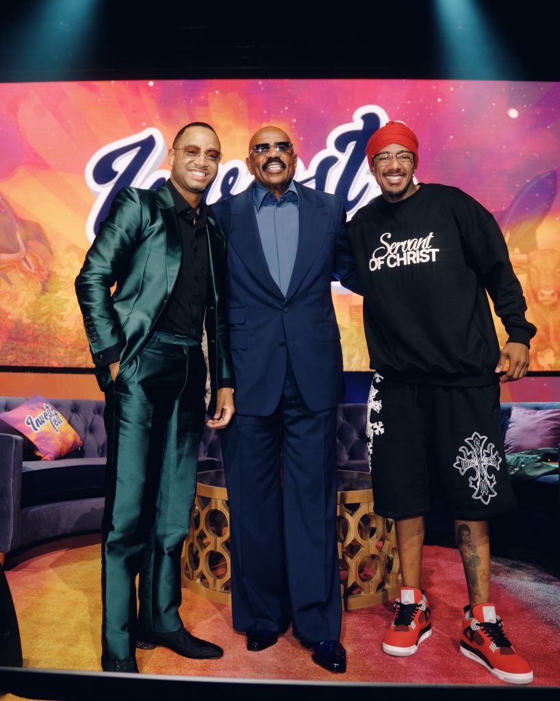 Three men posing together on a colorful stage, one wearing a "Servant of Christ" sweatshirt.