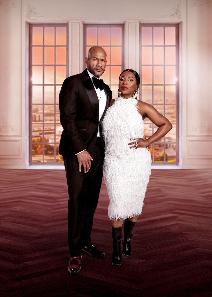 A well-dressed couple posing in a formal setting with a cityscape visible through large windows behind them.