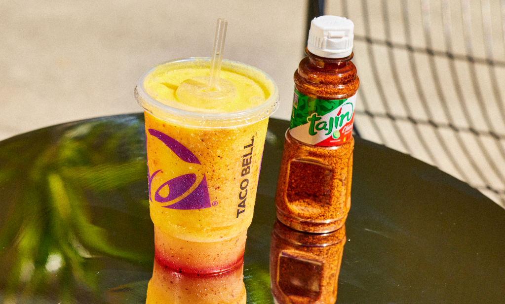A yellow and red smoothie drink with a Taco Bell logo, next to a bottle of Tajin seasoning.