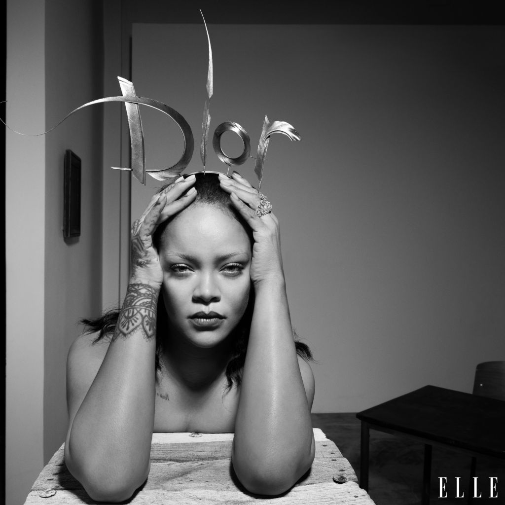 A black and white portrait of a woman with tattoos on her arms, holding scissors above her head in a dramatic pose.