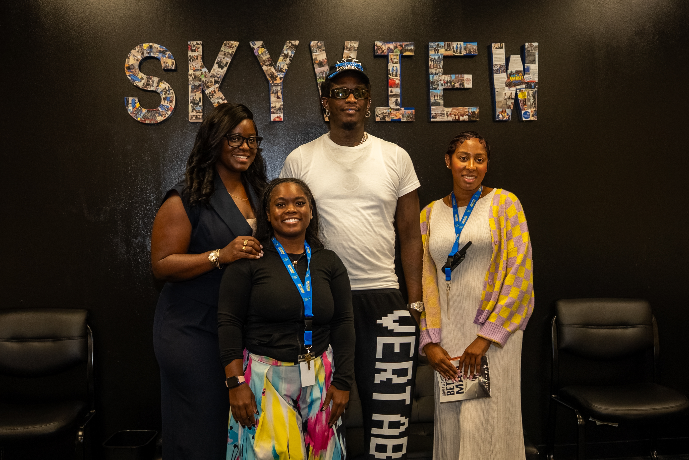 Four people standing in front of a large "SKYVIEW" sign made up of collaged images.