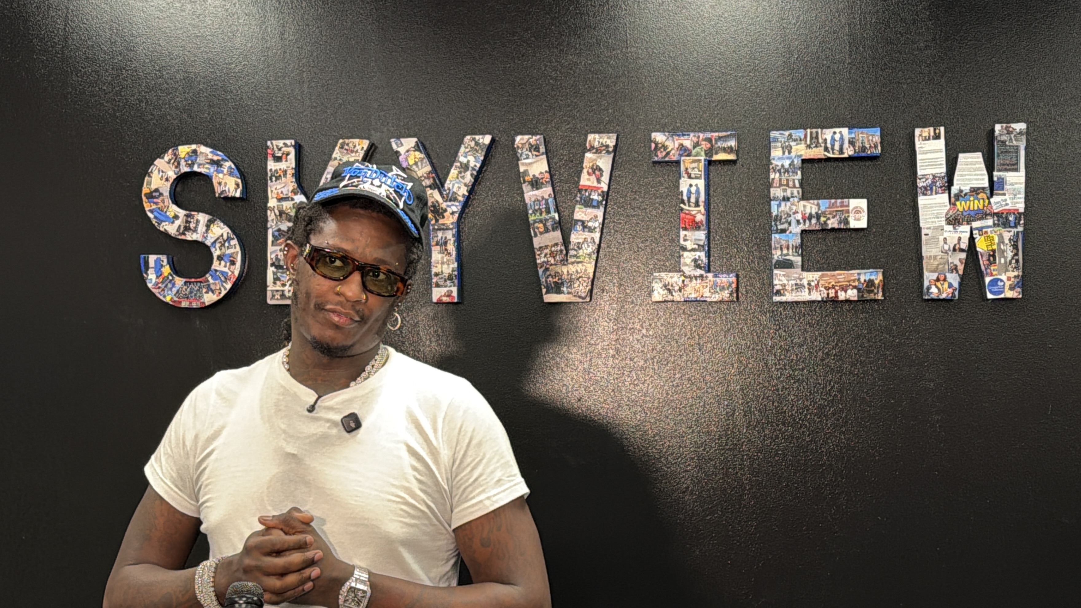 A man wearing sunglasses and a baseball cap stands in front of a wall with the text "SKYVIEW" displayed prominently.