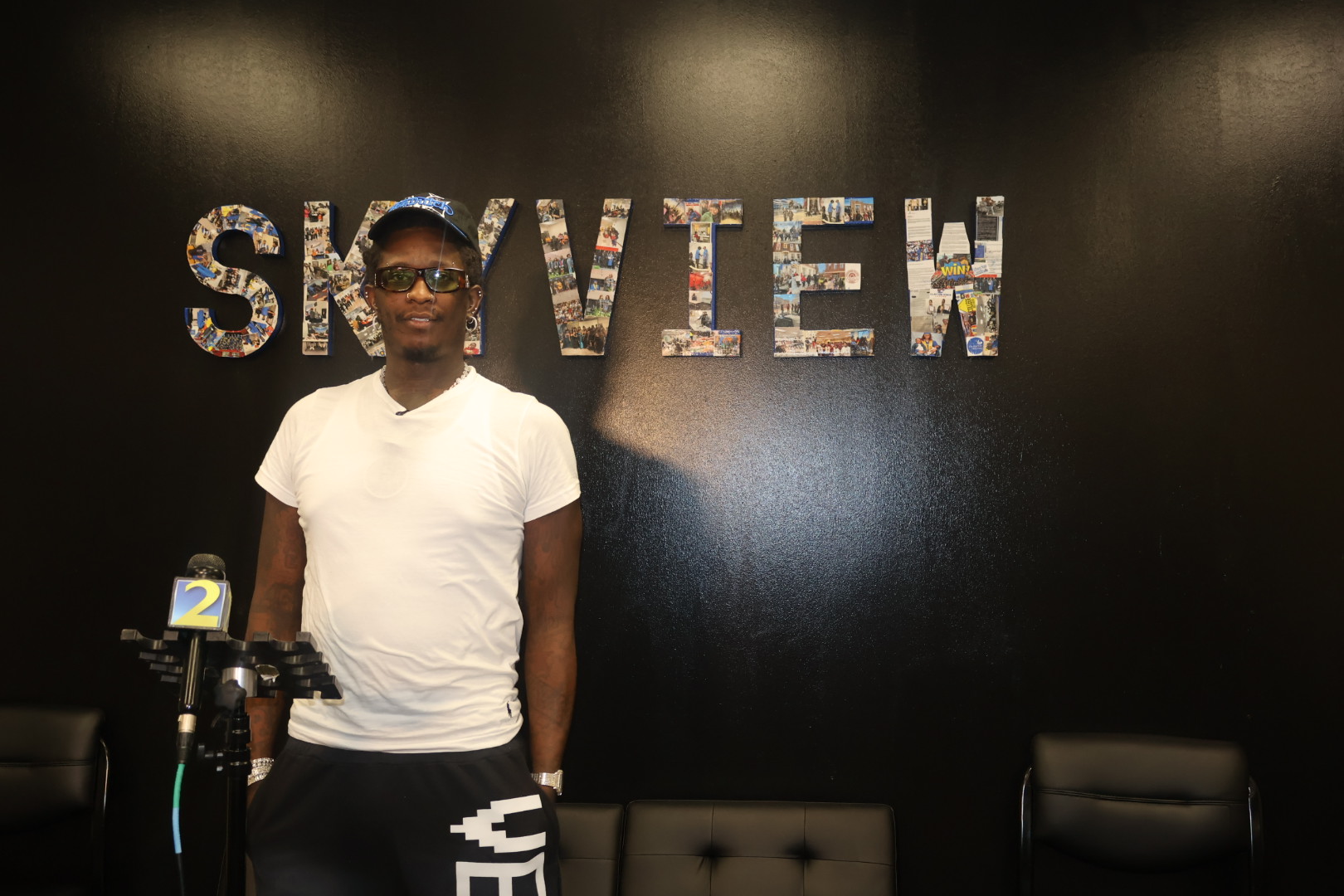 A person wearing a white t-shirt and sunglasses standing in front of a wall with the word "SKYVIEW" displayed in large letters.