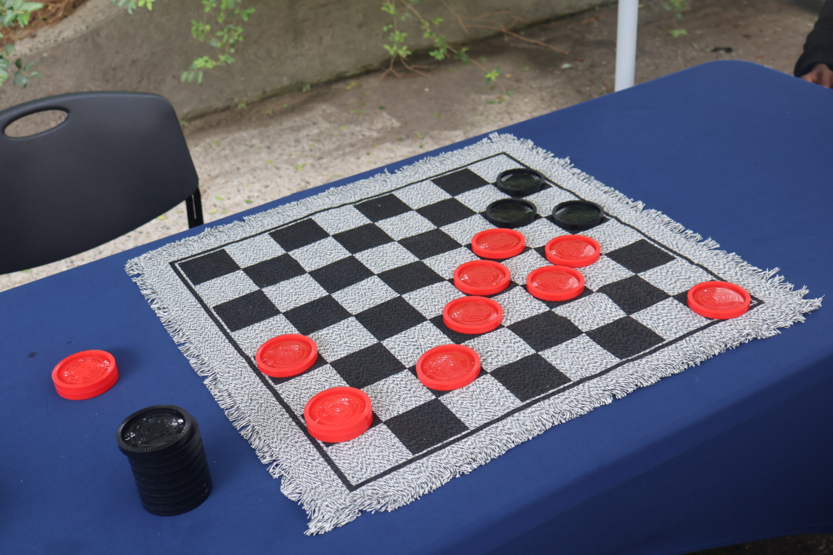 A blue table with a checkerboard game board and red and black game pieces on it.
