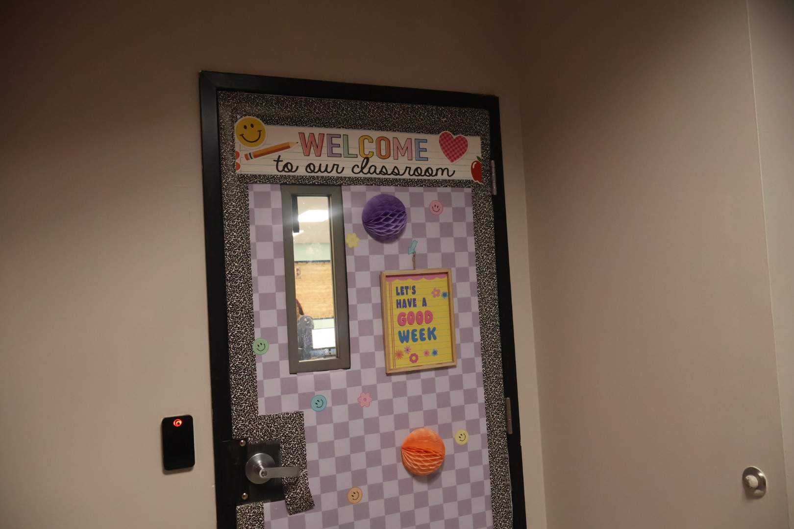 Welcome to our classroom, a cheerful and inviting space with a colorful bulletin board displaying a "Welcome" sign, smiley faces, and a message encouraging a "Good Week".