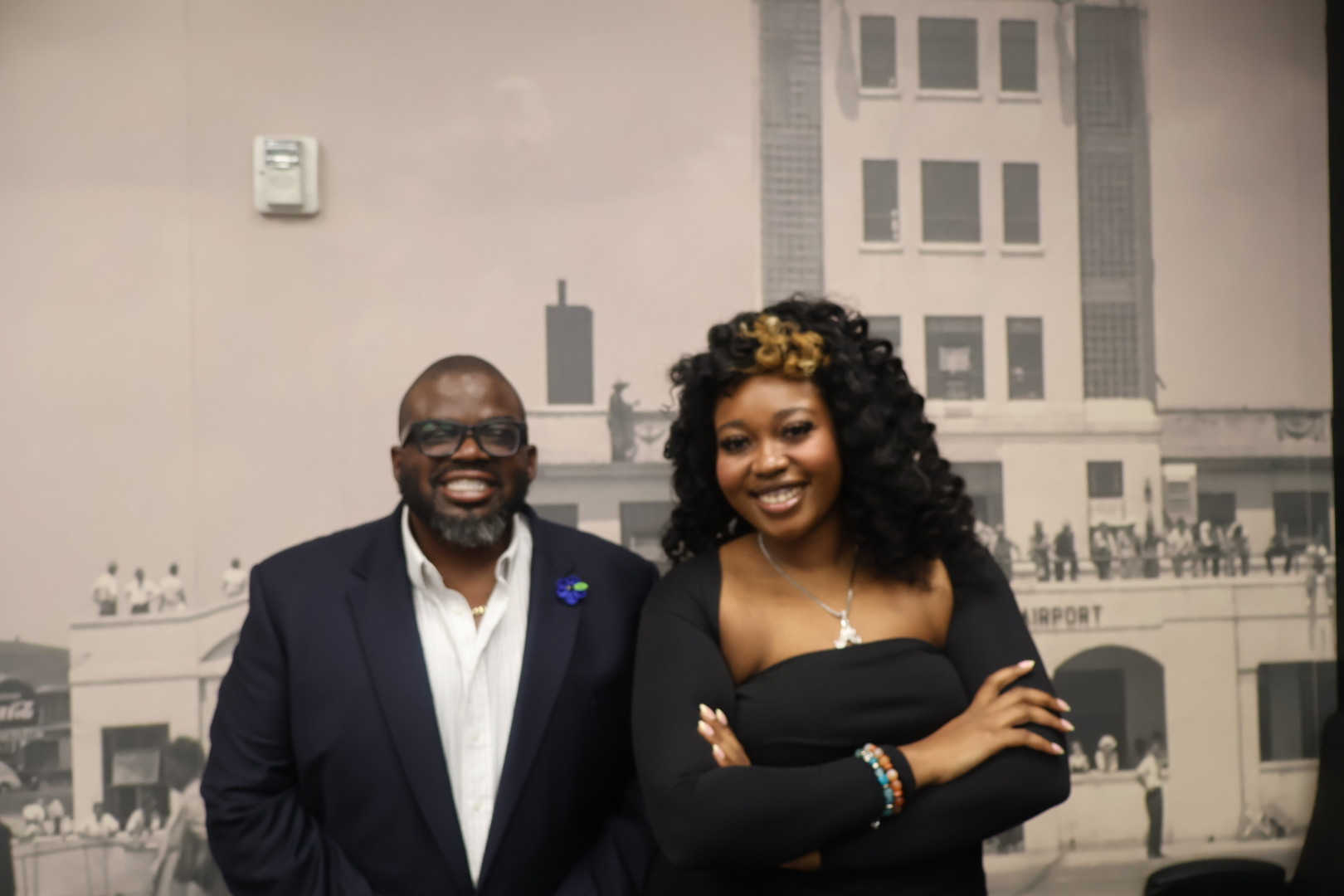 A smiling man and woman standing together in front of a city skyline backdrop.