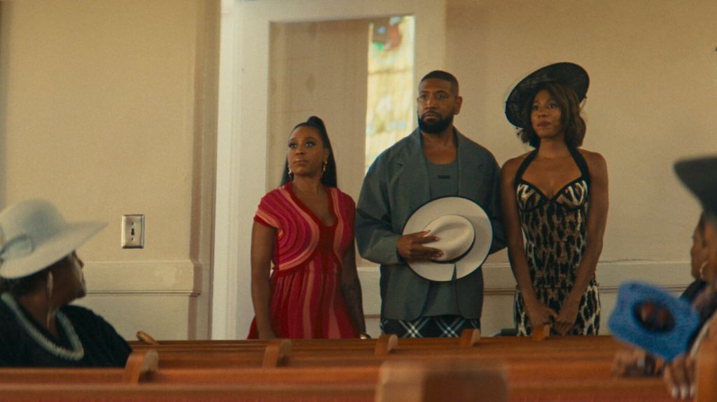 Three people standing in a doorway, one wearing a red dress, one wearing a hat, and one wearing a leopard print dress.