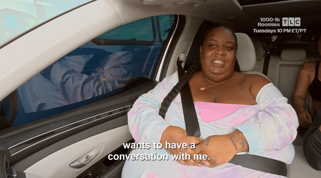 A smiling woman in a pink top and white cardigan sits in a car, with the text "wants to have a conversation with me" overlaid on the image.