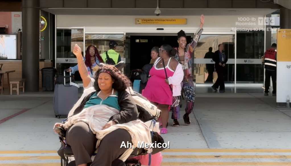 A group of people, some with their arms raised, standing in an airport terminal with a sign that says "Llegadas internacionales" (International Arrivals).