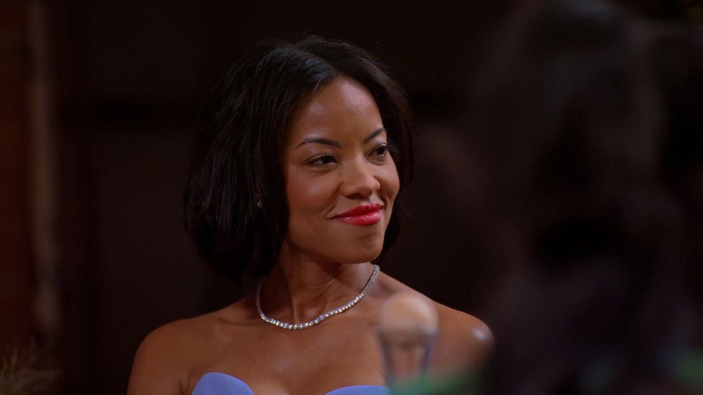 A smiling woman with dark hair wearing a blue dress and a diamond necklace.