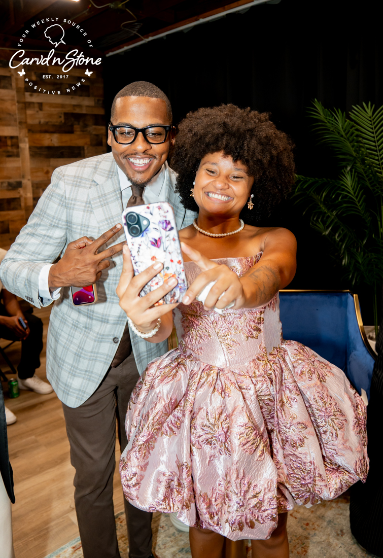 A smiling couple posing for a selfie, with the woman wearing a pink patterned dress and the man wearing a gray suit. The image includes the "Candid Stone" logo.