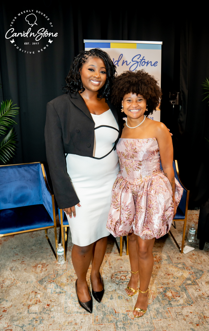 Two women posing in front of a Candigstone backdrop, one wearing a white dress and the other a pink floral dress.