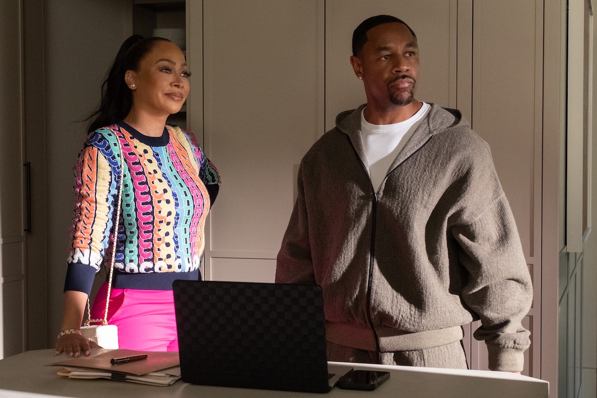 Two people, a woman in a colorful patterned jacket and a man in a gray sweater, standing in front of a laptop on a table.