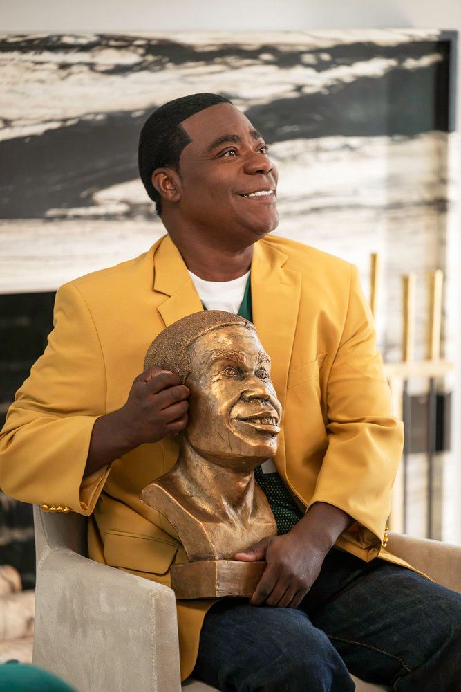 A smiling man in a yellow jacket holding a bronze bust of a face.